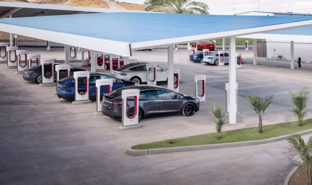 En stor Tesla Supercharger-station med flera bilar som laddar under ett tak.